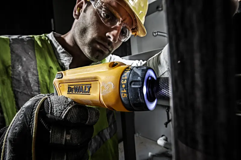 Personne utilisant un tournevis DEWALT DCF680G2 jaune avec gant dans un environnement industriel.